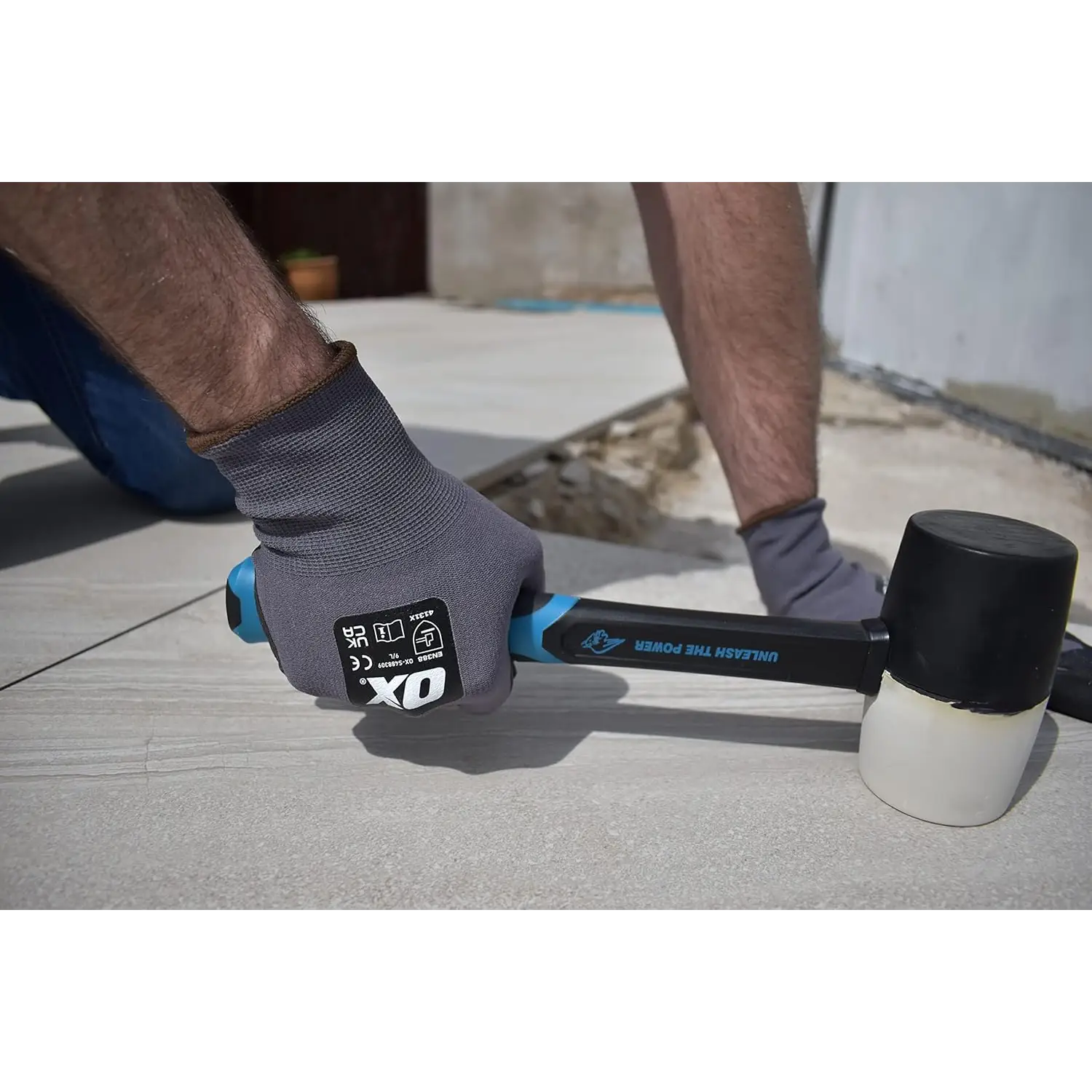 Mână cu mănușă purtând ciocan cauciuc combinat OX Trade cu mâner din fibră de sticlă