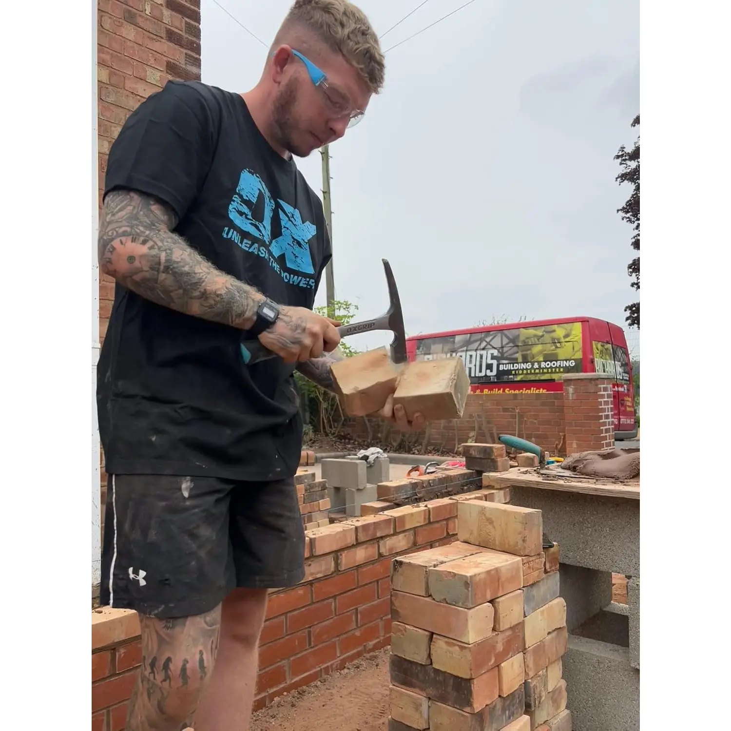 Bărbat cu tatuaje, purtând ochelari de protecție, folosind ciocan zidarie OX Pro otel forjat cu soft grip