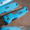Cutter pliabil OX PRO — detaliu mâner, buton de eliberare și clemă