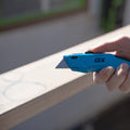 Cutter retractabil OX PRO ținut în mână, cu lama scoasă, pe șantier