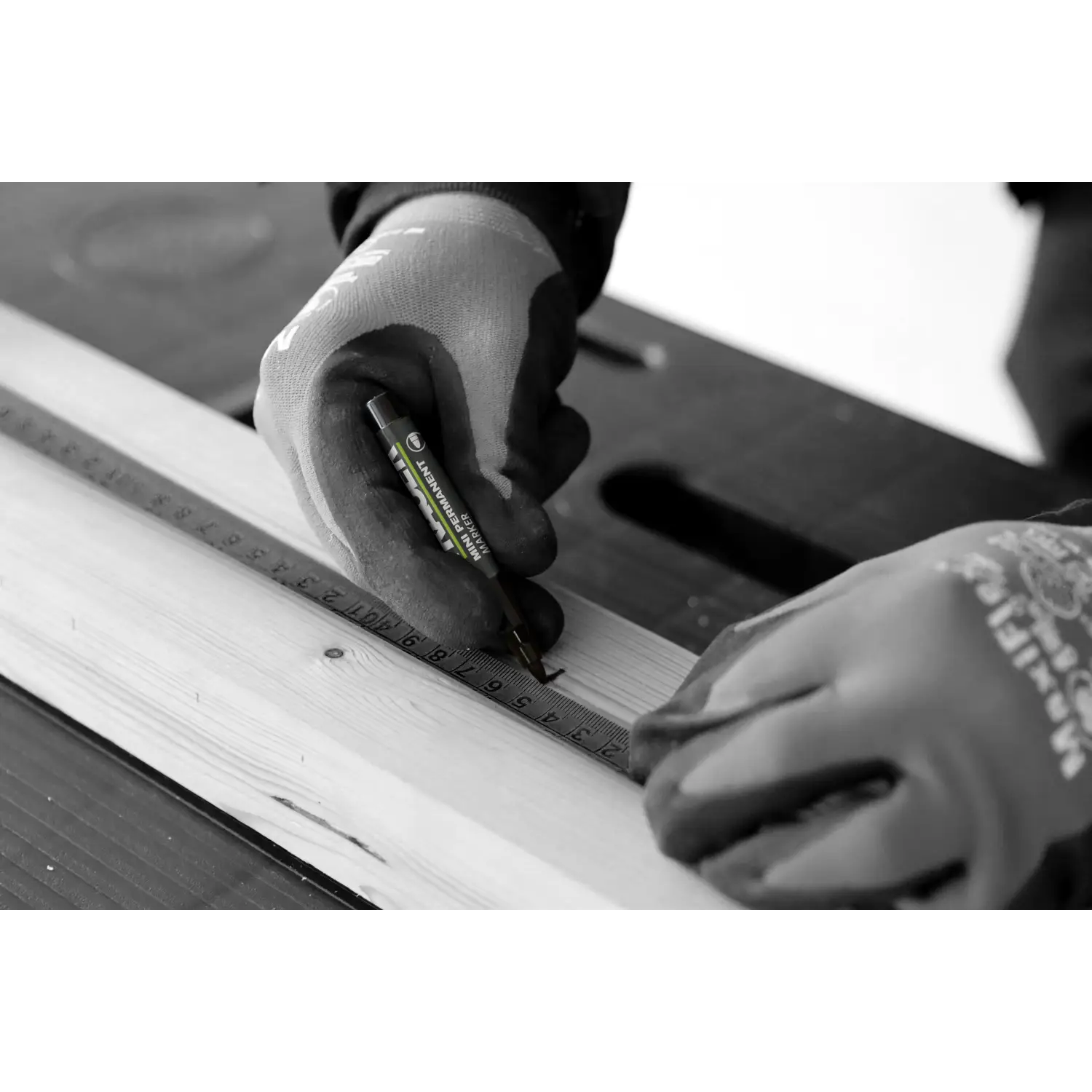 Mână cu mănușă de lucru ținând un marker permanent mini negru și riglă pe lemn