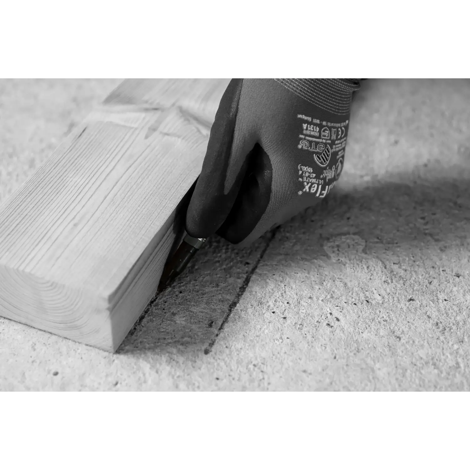 Mână cu mănușă ținând un marker permanent mini negru TRACER pe o suprafață de beton